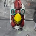 Finished hand-painted Payday 2 chicken mask, front view — red comb and wattle, yellow beak, teal eye rings