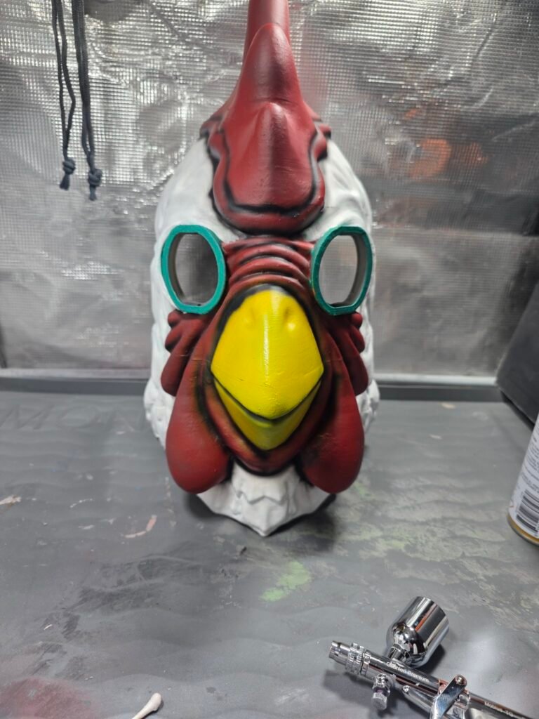 Finished hand-painted Payday 2 chicken mask, front view — red comb and wattle, yellow beak, teal eye rings